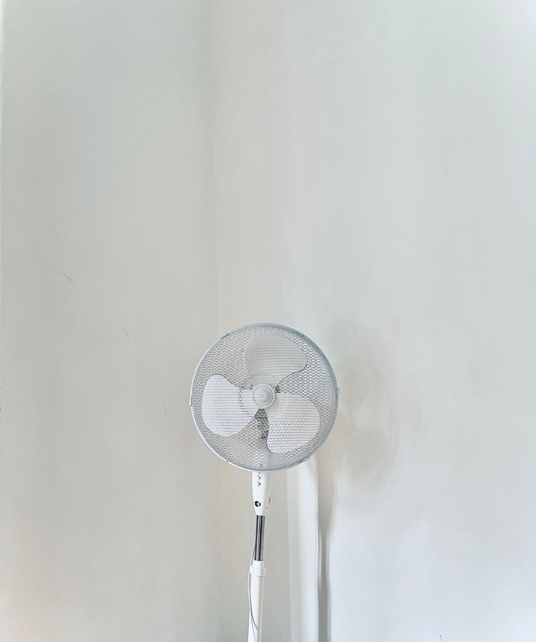 a stand fan beside a white wall