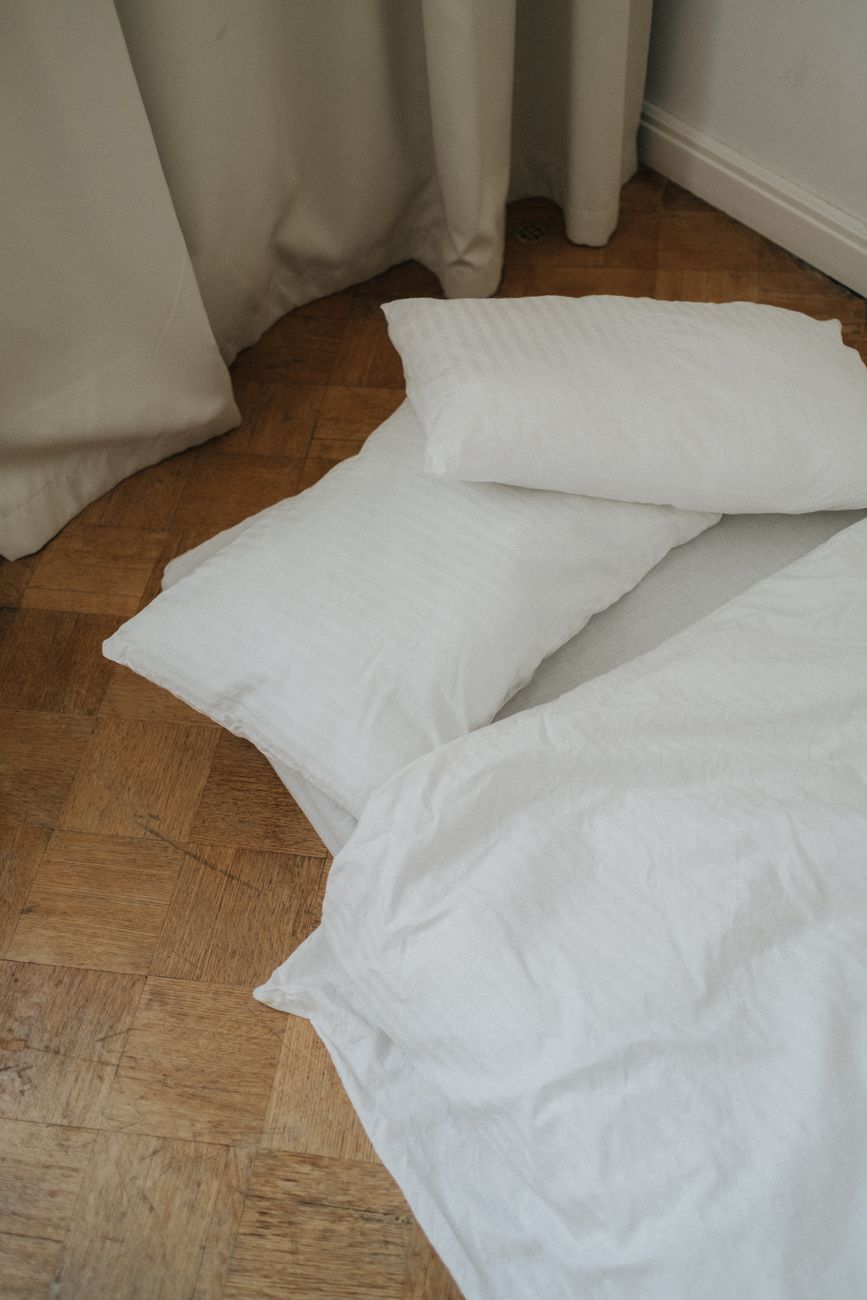 a bed with linens and pillows on the wooden floor